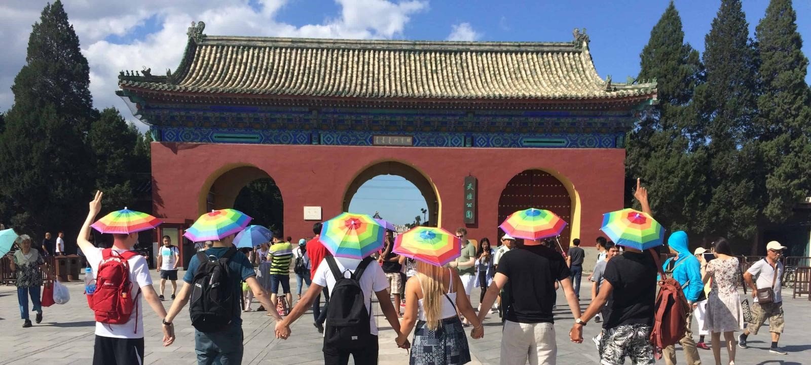 Students wearing rainbow umbrella hats at the entrance to a temple in China.