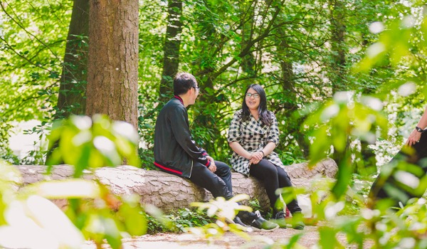 Two students sit on a log on the Woodland Walk